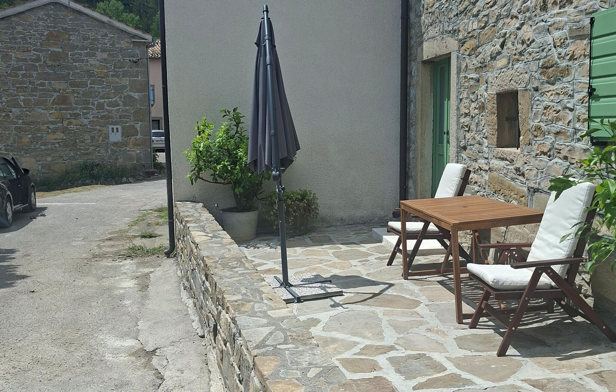 Un patio al aire libre con suelo de piedra, una mesa y dos sillas, una planta en maceta y un parasol plegable.