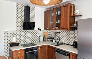 A kitchen with patterned backsplash, wooden cabinets, a built-in dishwasher, and a hanging light fixture.