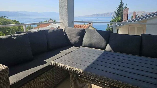 Un espace extérieur aménagé avec des sièges, offrant une vue sur la mer et les montagnes.