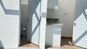 Una habitación con una puerta blanca, un lavamanos pequeño y suelo de madera.