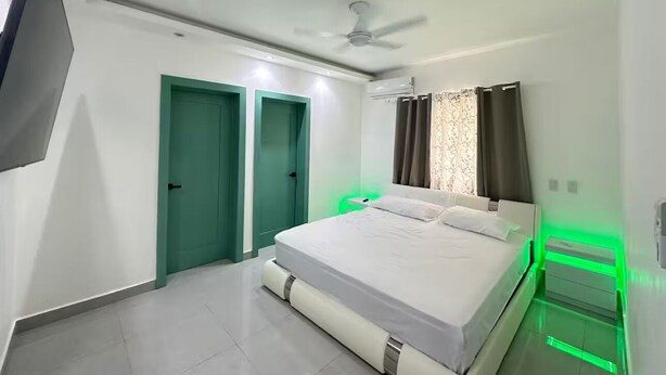 Un dormitorio moderno con cama, ventilador de techo e iluminación ambiental verde.