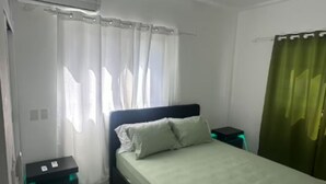 Un dormitorio con cama, ventilador de techo, mesita de noche y cortina verde.