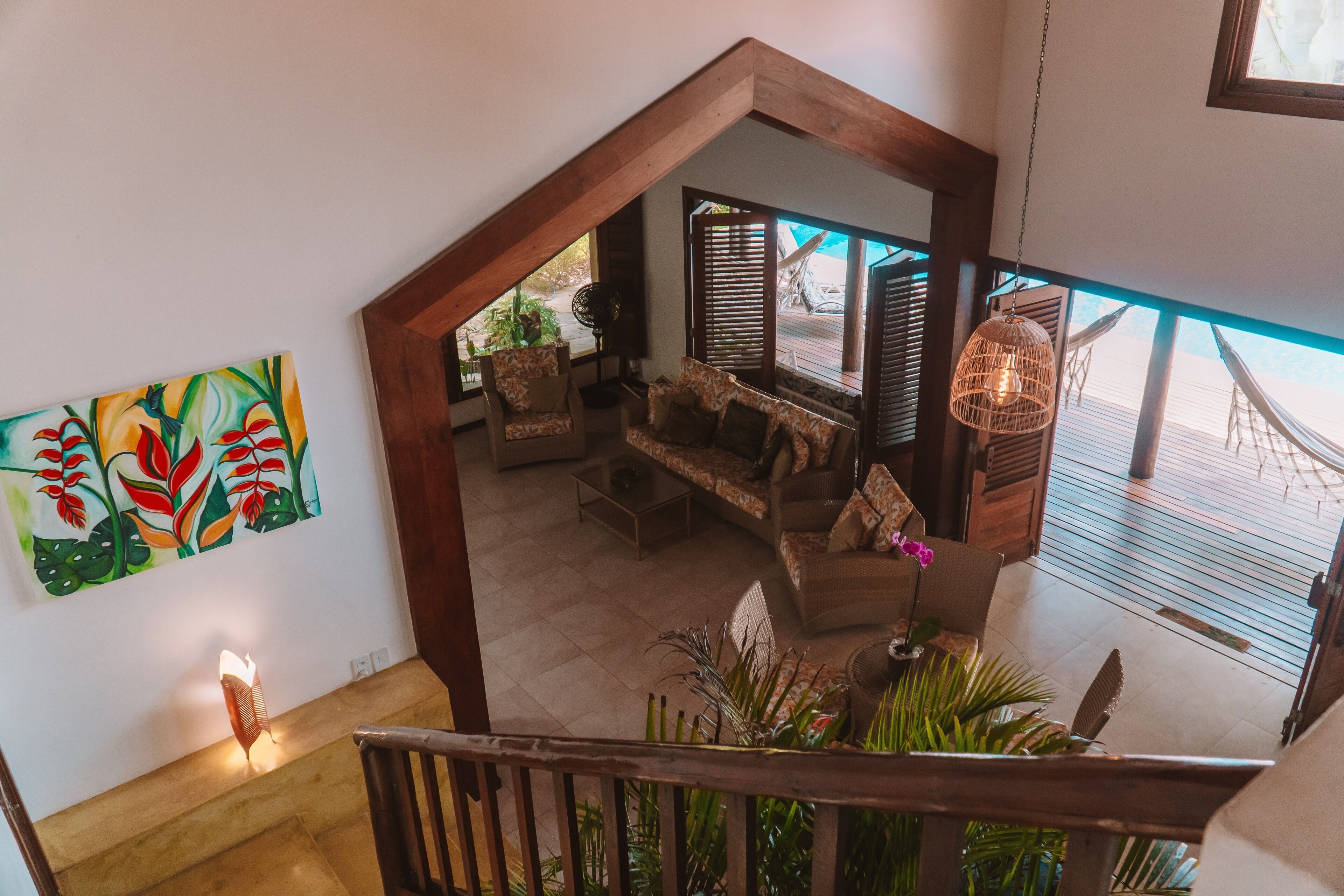 A staircase leading to a living area with a view of the outdoors, a colorful painting on the wall, and a hanging light fixture.