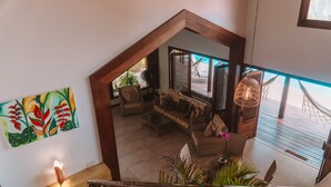 Una escalera conduce a una sala de estar con vistas al exterior, un cuadro colorido en la pared y una lámpara colgante.