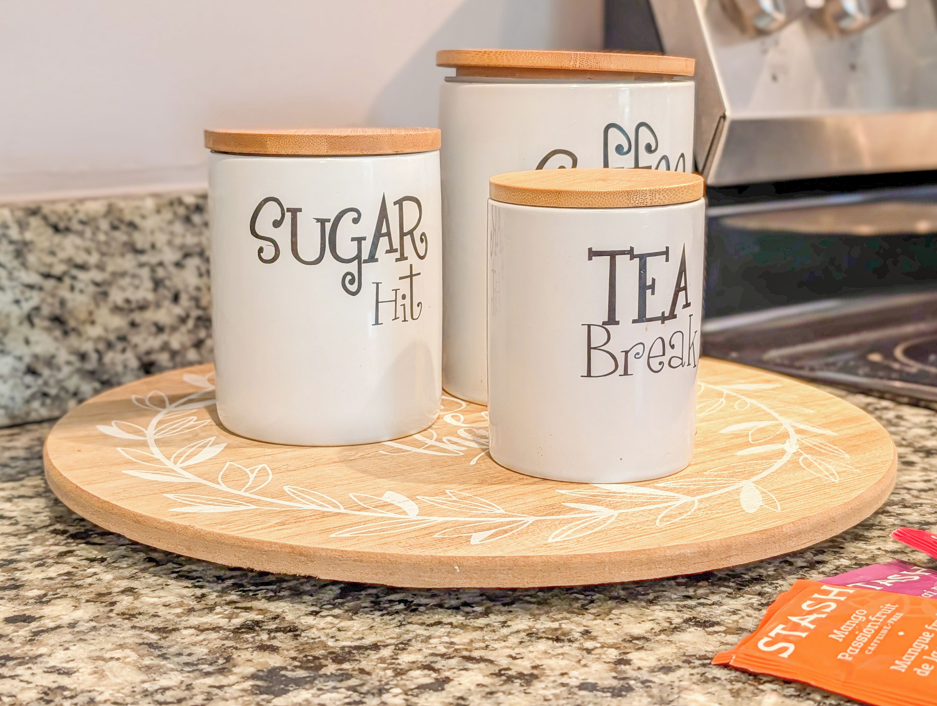 Two white containers with wooden lids on a wooden board, labeled 'SUGAR Hit' and 'TEA Break.'