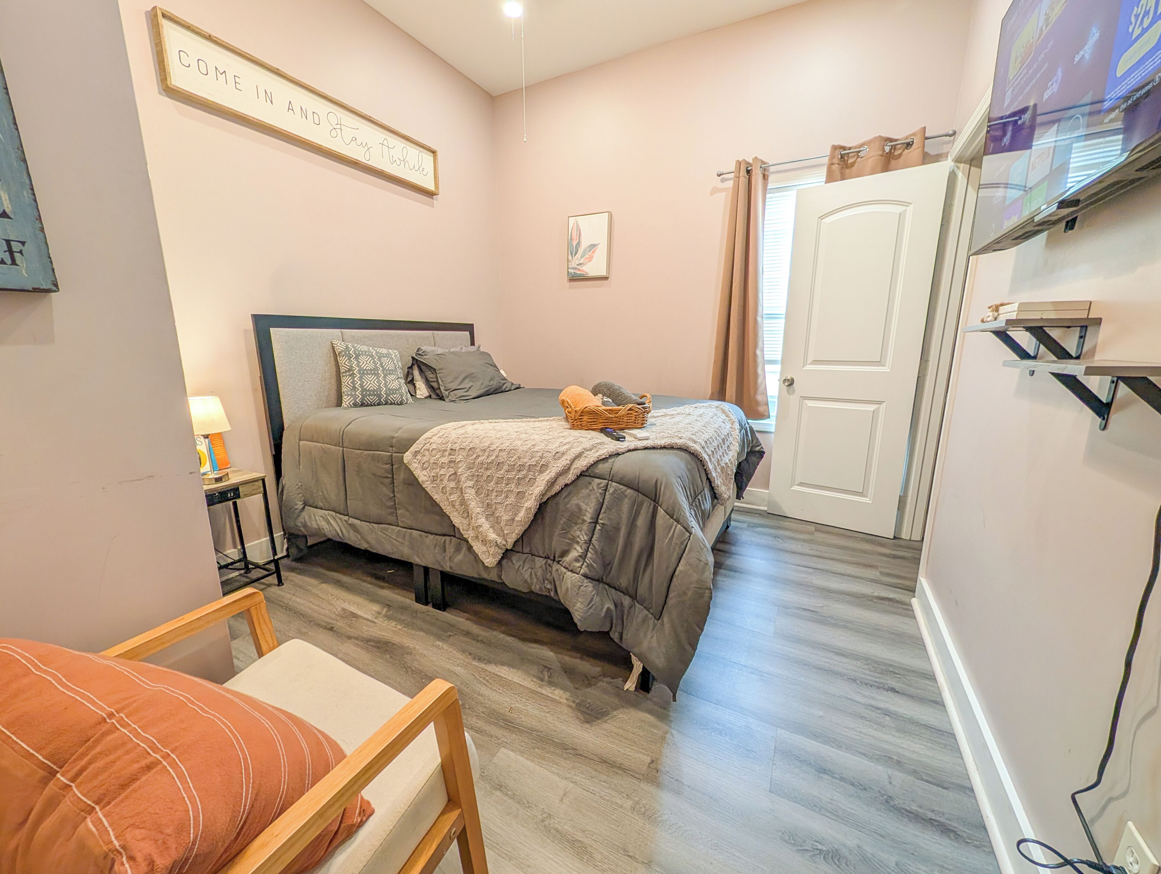 Une chambre à coucher comprenant un lit, une chaise, une table de chevet, une porte et une étagère fixée au mur.