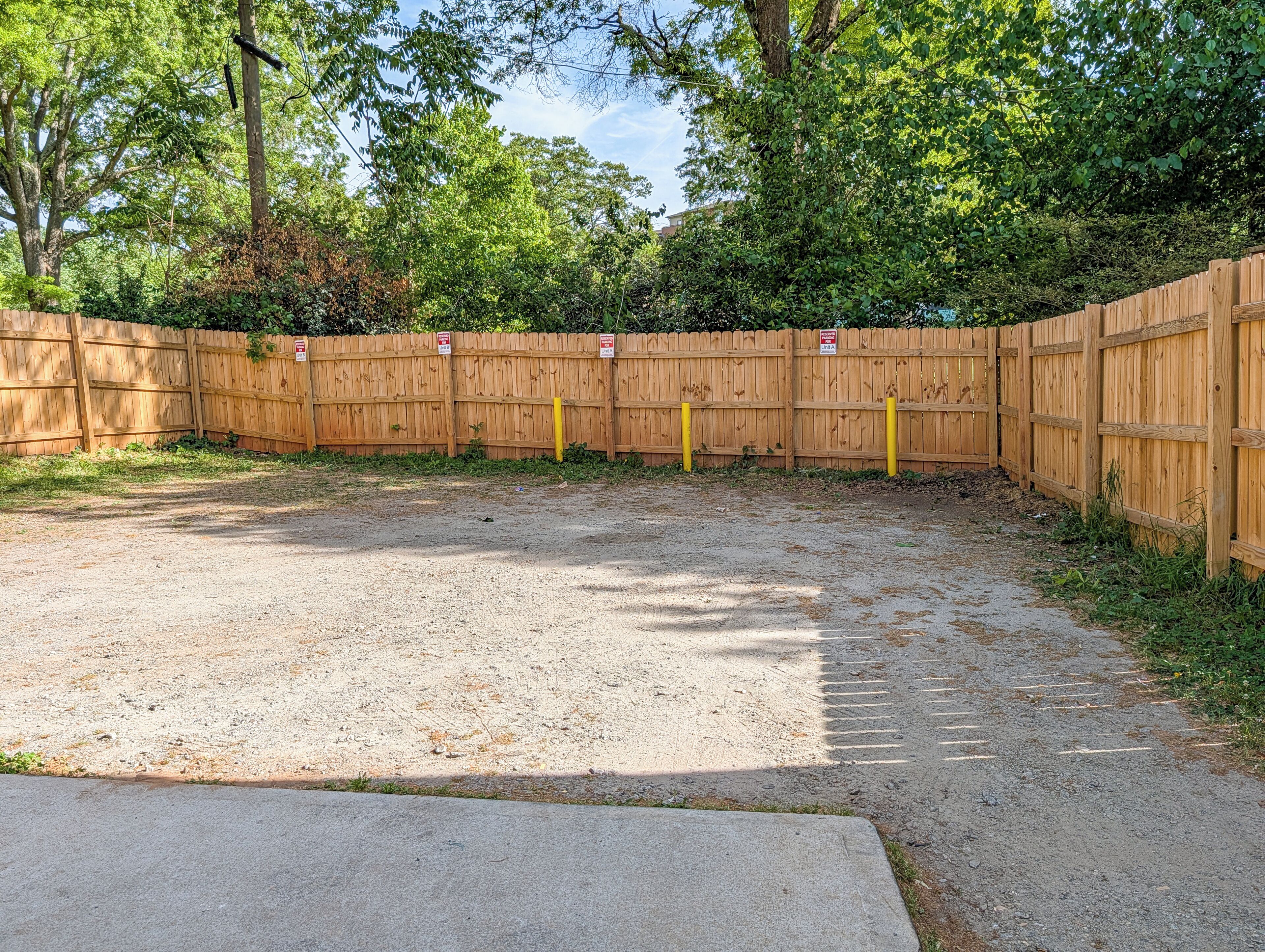 A fenced outdoor area with a gravel surface, surrounded by trees and a wooden fence.