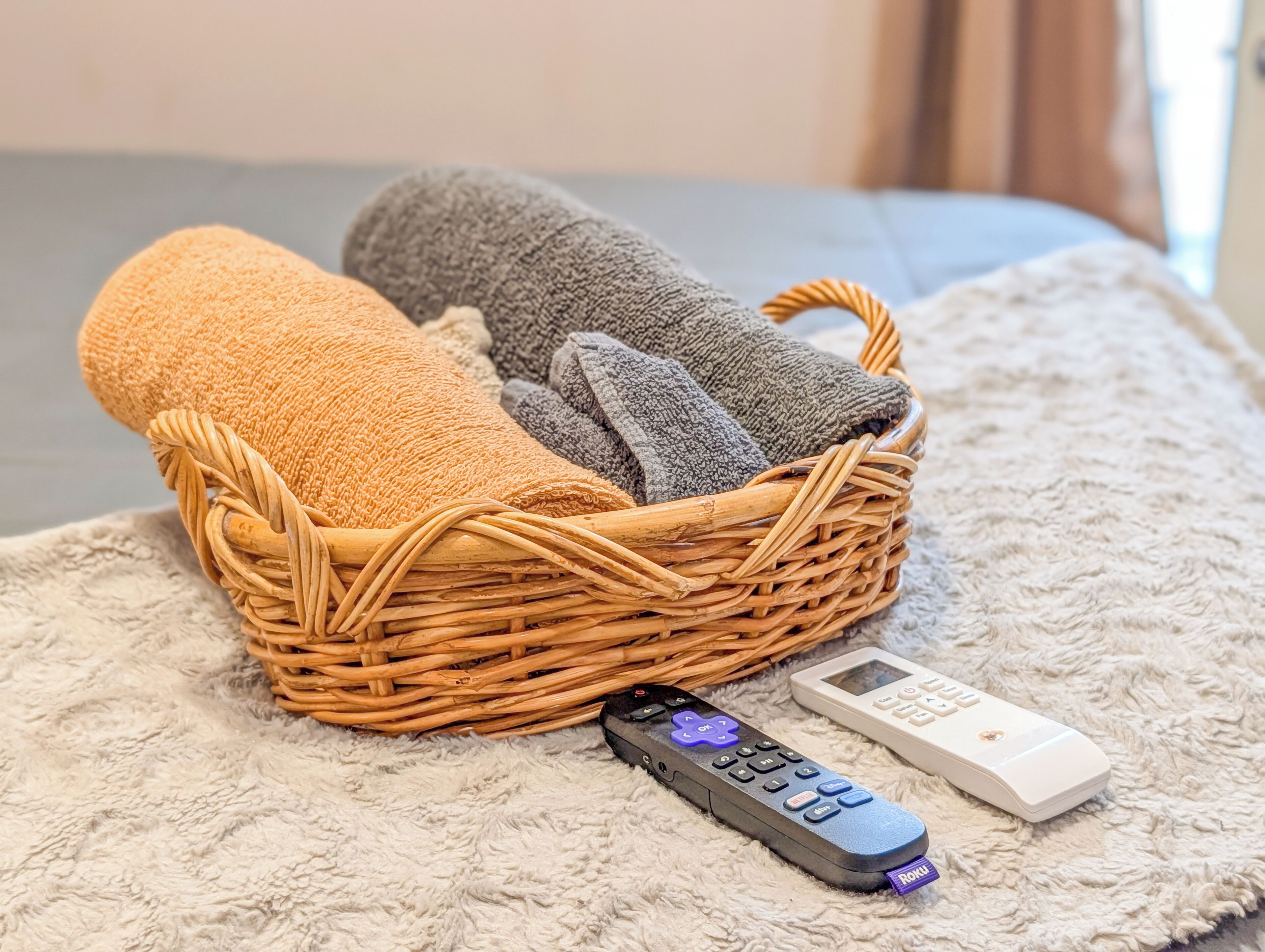 A wicker basket with folded towels and a remote control on a textured surface.