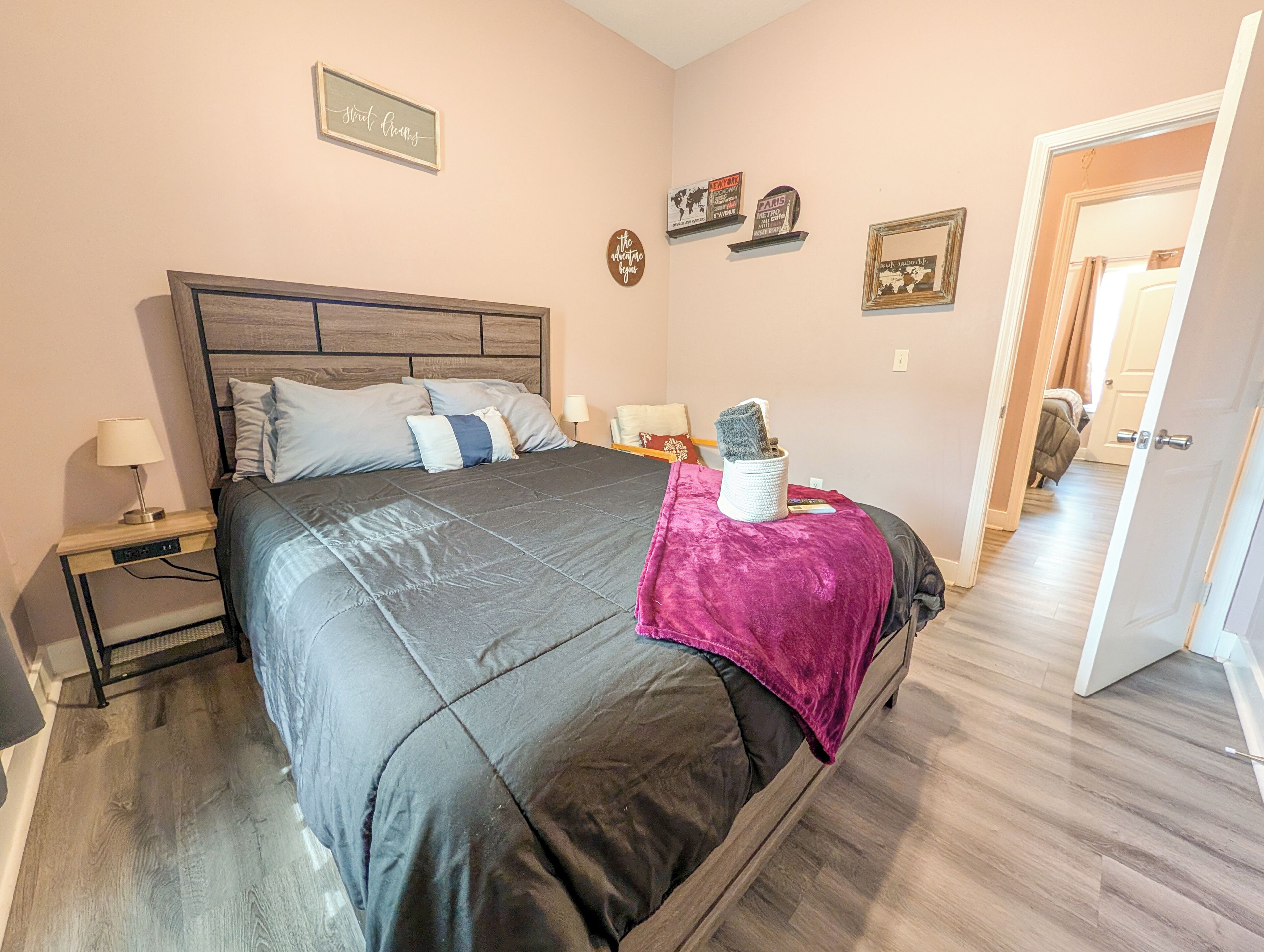 A bedroom with a bed, bedside tables, a nightstand, a lamp, a blanket, and wall decorations.