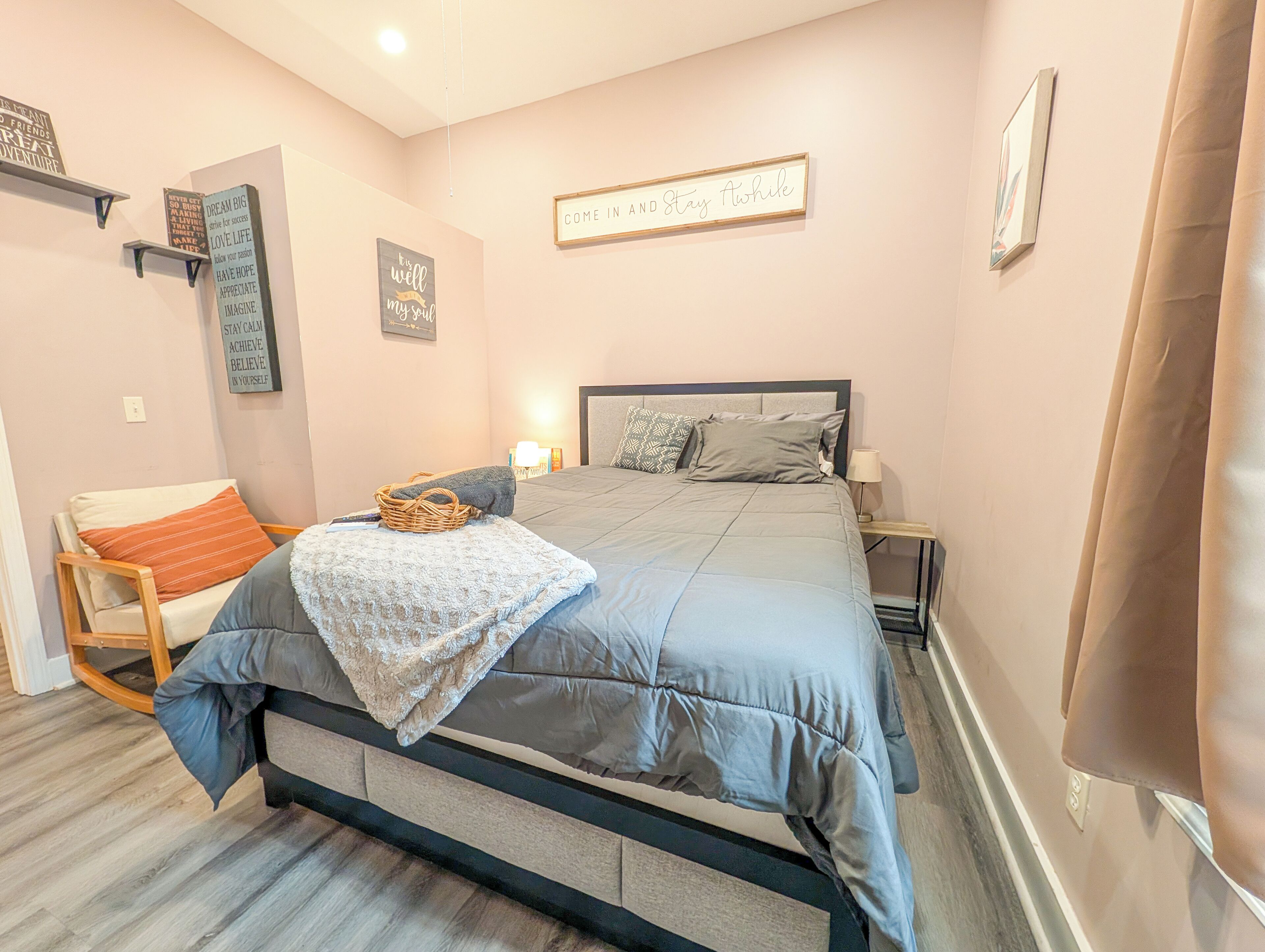 A bedroom with a bed, a chair, a nightstand, and motivational wall art.