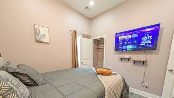 Un dormitorio con una cama, un televisor montado en la pared y una puerta que da a otra habitación.