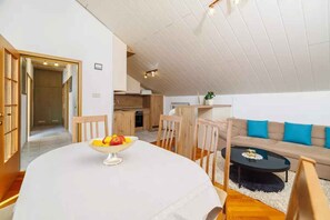 Ein modernes Wohnzimmer mit einem runden Esstisch, einer Couch und einer Küchenzeile im Hintergrund.