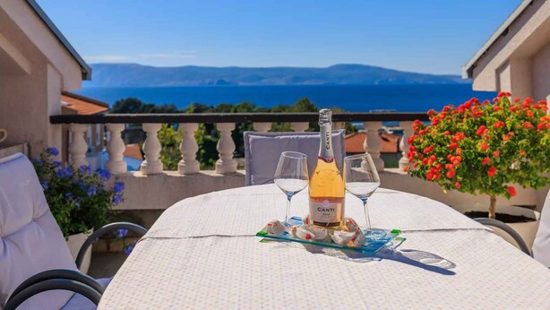 A table set with a bottle of Canti Rosé wine, two wine glasses, and a plate of appetizers on a balcony overlooking a scenic view of the sea and mountains. - Holiday flat with terrace and sea view (Novi Vinodolski)