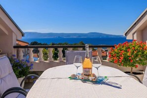 A table set with a bottle of Canti Rosé wine, two wine glasses, and a plate of appetizers on a balcony overlooking a scenic view of the sea and mountains. - Holiday flat with terrace and sea view (Novi Vinodolski)