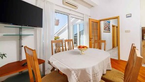 A dining area with a round table, chairs, a TV, and a window with curtains. - Holiday flat with terrace and sea view (Novi Vinodolski)