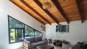 Un vaste salon doté d’un haut plafond en bois, de grandes fenêtres et d’un téléviseur à écran plat fixé au mur.