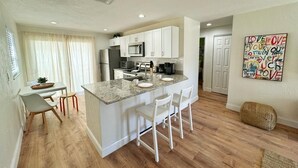 A modern kitchen with white cabinets, a granite countertop, and a bar area with stools. - NEW Gorgeous Sunshine-Up 6 Guests-Private Backyard (Port Orange)