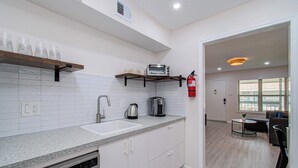Ett modernt kök med vita skåp, en bänkskiva i granit, en inbyggd diskmaskin, en kaffebryggare och en brödrost. En brandsläckare är monterad på väggen.