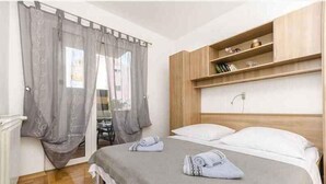 A bedroom with a bed, grey curtains, a wooden headboard, and a shelf with books. - Holiday apartment Apartment A2 (2+2) Ground floor (Srima)