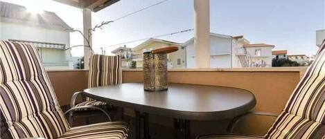 A covered outdoor seating area with striped upholstered chairs and a round table, overlooking a residential neighborhood.