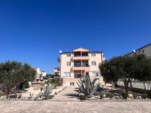 A multi-story residential building with balconies and satellite dishes, surrounded by landscaped areas with cacti and trees. - Holiday Apartment Milenko Ivic 2 (4+0) (Vodice)