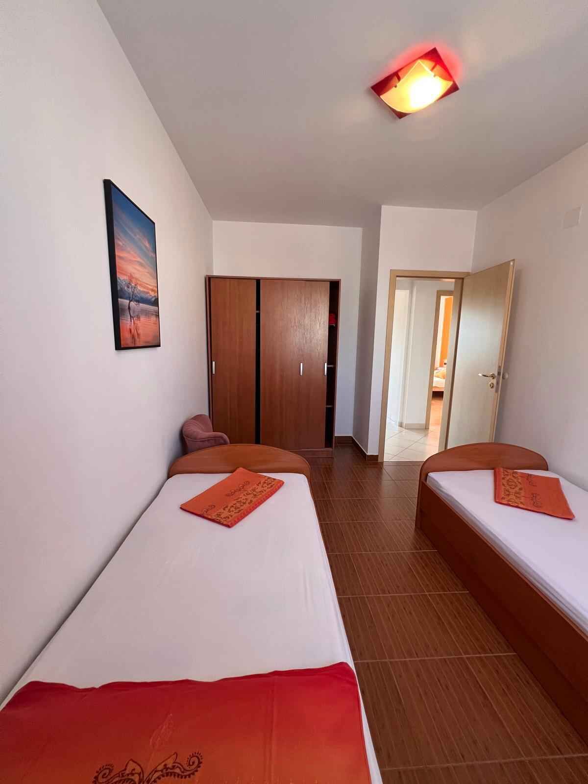 Ein Zimmer mit zwei Einzelbetten, einem Holzschrank, einer Tür zu einem weiteren Raum und einem Bild an der Wand.