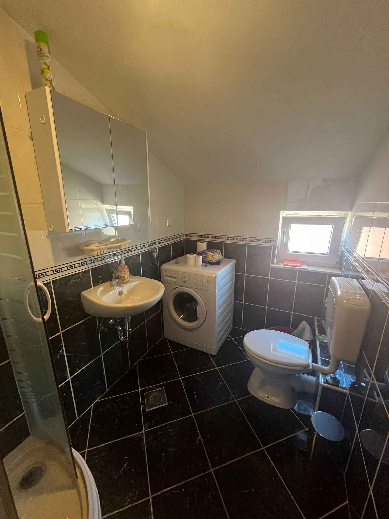A compact bathroom with a sink, washing machine, and toilet.