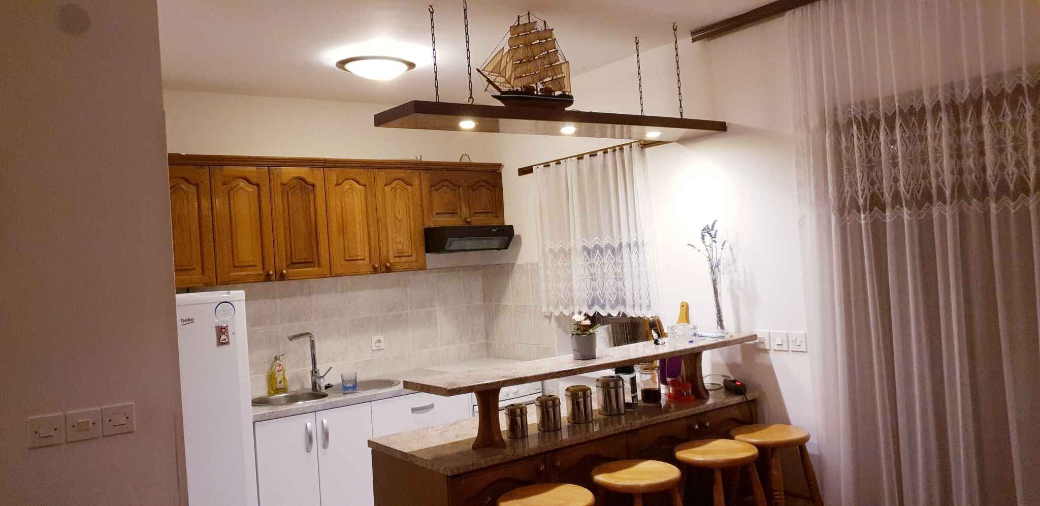 A kitchen with wooden cabinets, a built-in stove, a hanging ship decoration, and a bar area with stools.