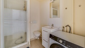 A compact bathroom with a glass shower enclosure, a toilet, a sink, and a washing machine.
