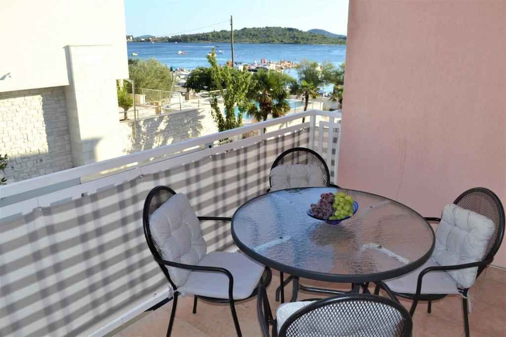 A balcony with a round glass table and four chairs, overlooking a coastal area with boats and buildings.