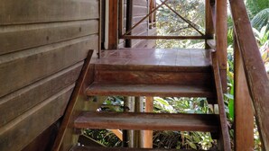 A wooden staircase leading to a covered porch with a view of lush greenery.