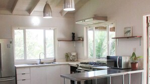 A modern kitchen with a central island, bar stools, a refrigerator, and a window overlooking greenery.