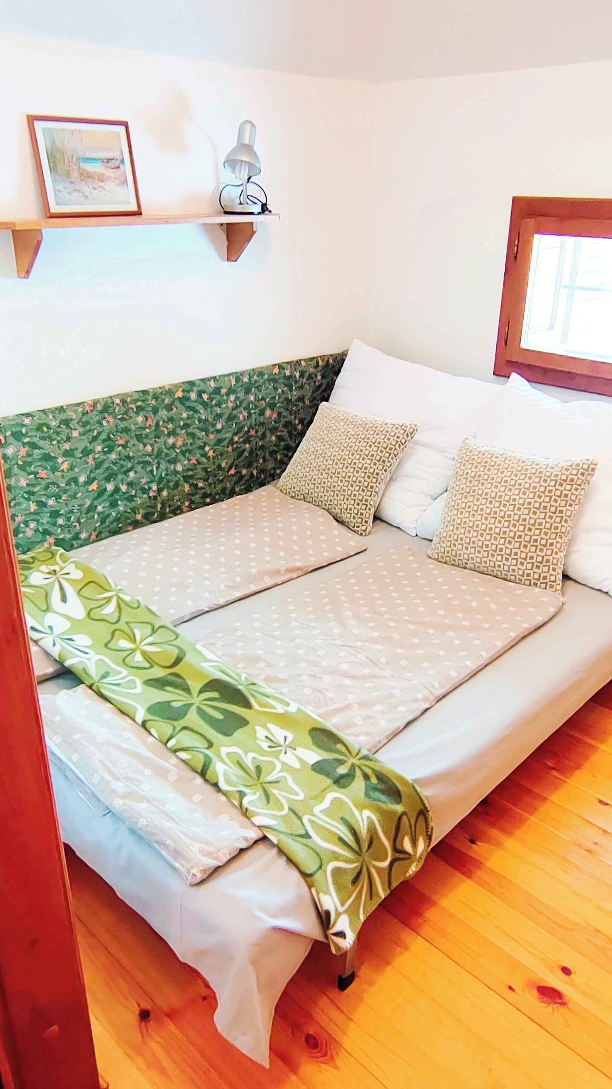 A bed with a green floral bedspread, two patterned pillows, and a wall-mounted lamp.