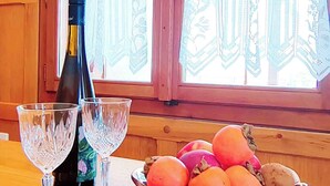 Un tavolo di legno con una bottiglia di vino, due bicchieri e una ciotola di frutta.