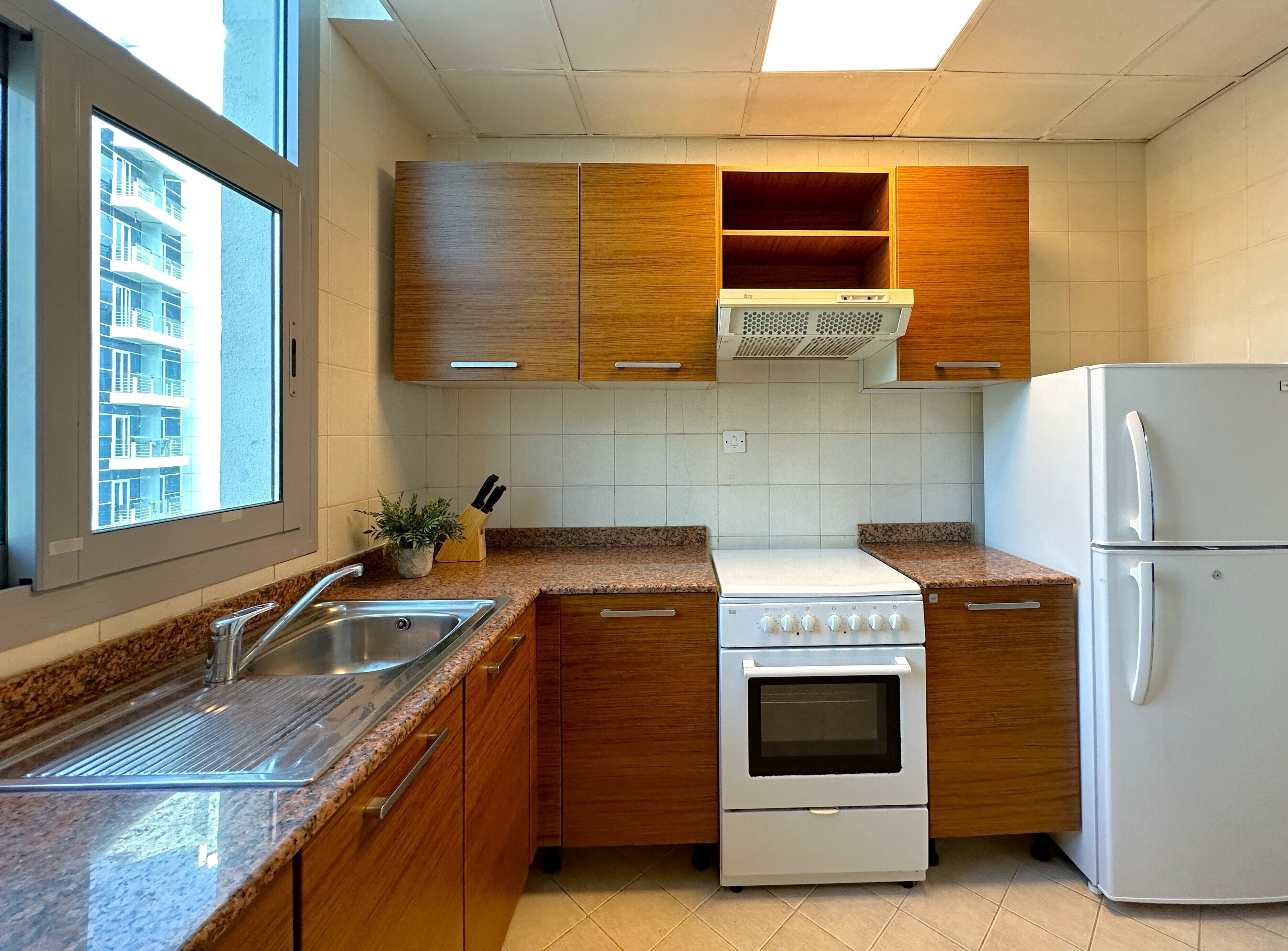 A kitchen with wooden cabinets, a white stove, a refrigerator, and a window with a view of a building.