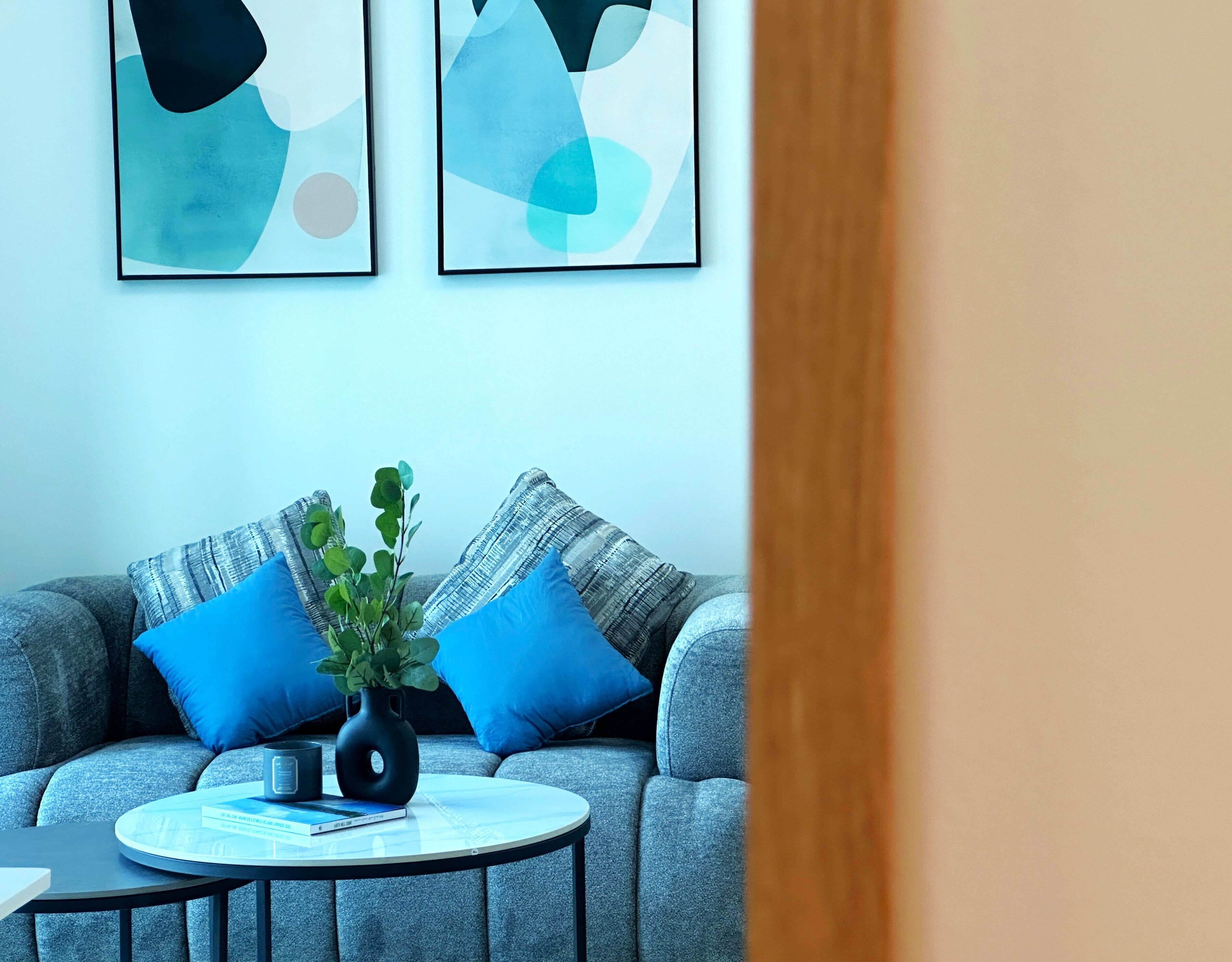 A modern living room with a grey sofa, blue cushions, a round coffee table, and a potted plant.