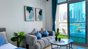 A modern living room with a grey sofa, blue cushions, a round coffee table, and a large window with a city view. - Luxury Brand New Studio  (Dubai)