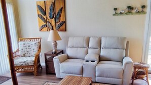 Uma sala de estar com sofá, duas mesas de madeira, uma cadeira, abajur e obras de arte na parede.