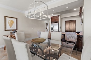 A dining area with a glass table, cushioned chairs, and a hanging light fixture. - Beach Front w/Wrap Around Balcony Free Pickleball Tides Unit 1101 (Miramar Beach)