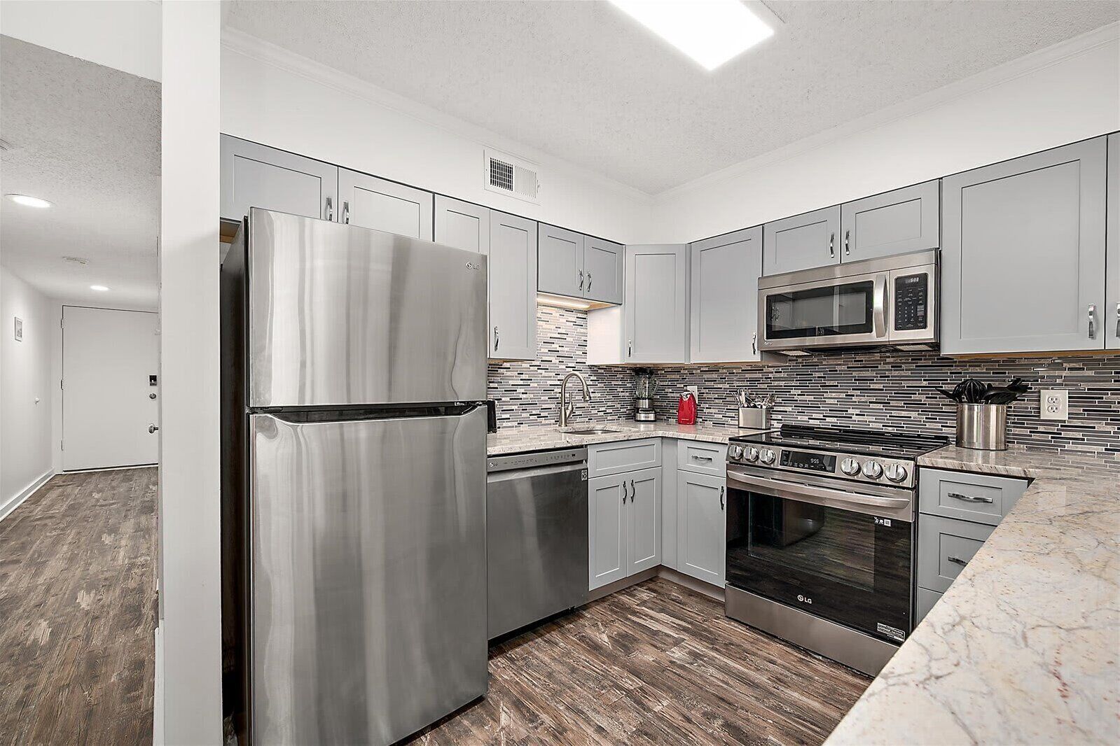 A modern kitchen with stainless steel appliances, grey cabinets, and a tiled backsplash.