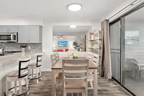A modern kitchen with white cabinets, a microwave, and a dining area with a wooden table and chairs. - Bayside Condo w/ Great Pool and Short Beach Walk (Ocean City)