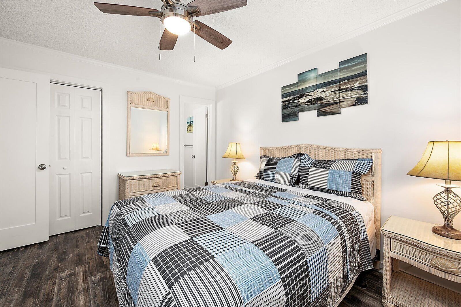 A bedroom with a bed, two bedside tables, a ceiling fan, a wall-mounted mirror, and a painting.
