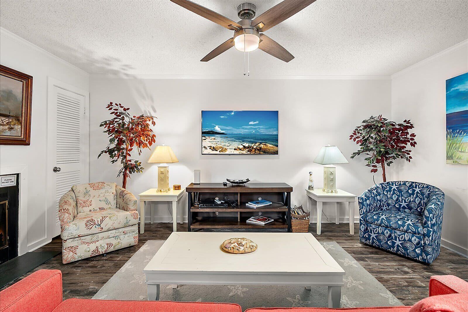Un salon avec une table basse blanche, deux fauteuils, un canapé, un téléviseur et un ventilateur de plafond.