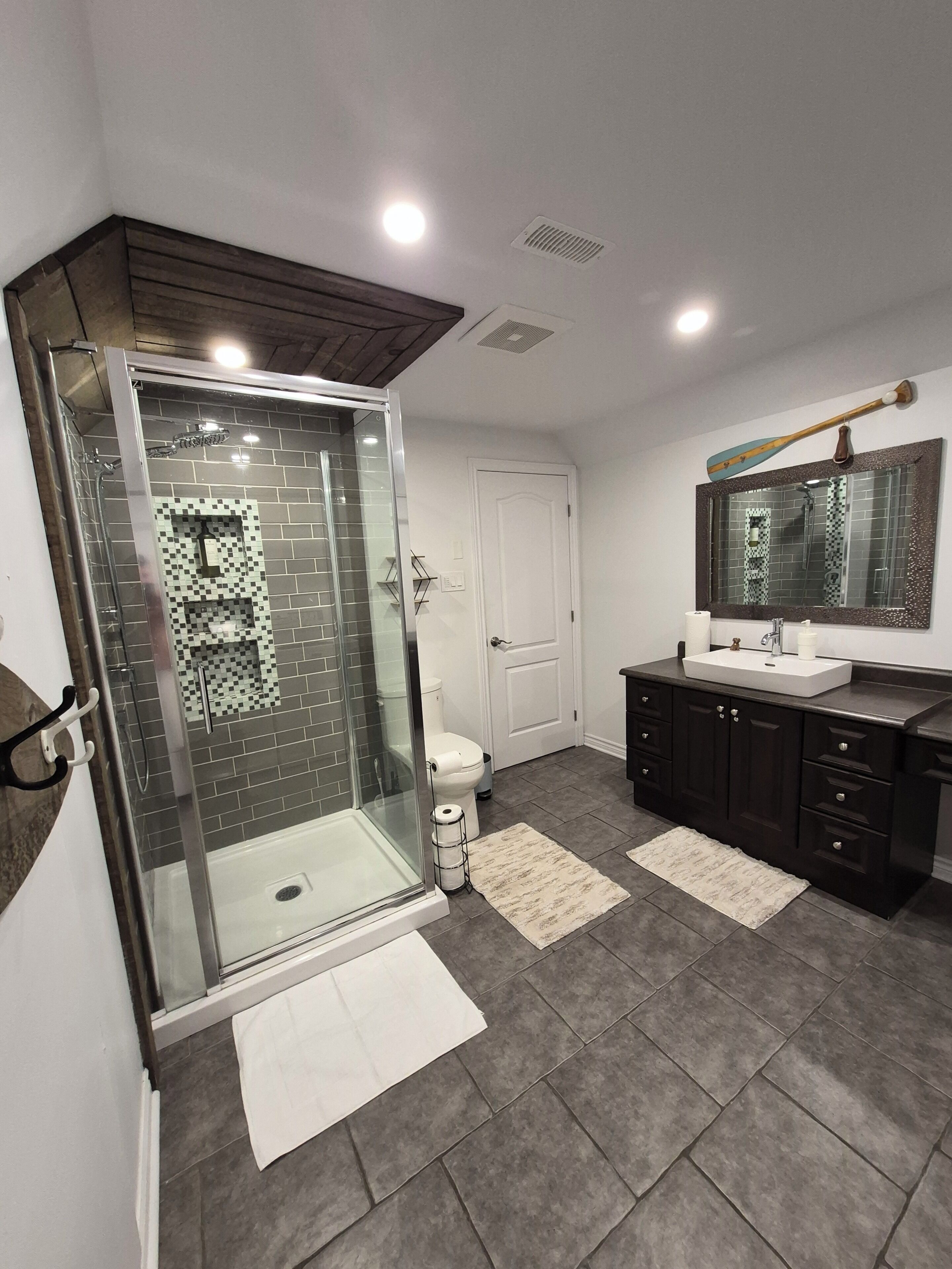 A modern bathroom with a glass-enclosed shower, a white toilet, a sink with a mirror, and dark-toned cabinets.