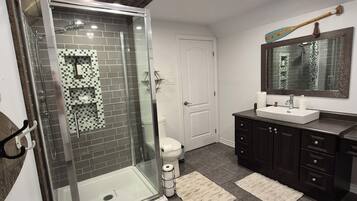 A modern bathroom with a glass-enclosed shower, a white toilet, a sink with a mirror, and dark-toned cabinets.
