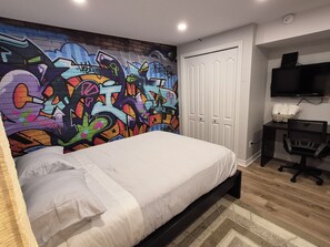 A bedroom with a colorful graffiti wall, a bed, a desk with a chair, and a TV mounted on the wall. - Spacious 1-bedroom basement unit (full bathroom/shared laundry) (Gatineau)