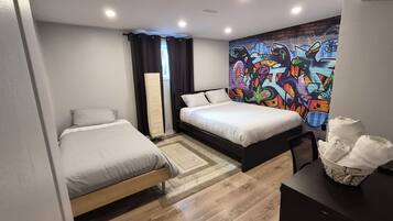 Un dormitorio con dos camas, un ventanal con cortinas, una pared con grafitis y un escritorio con una cesta.