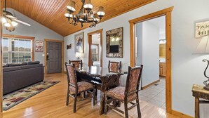 A spacious dining area with a wooden ceiling, a chandelier, and a large table surrounded by chairs. - Blue Sky Lodge  For 4 (Branson West)