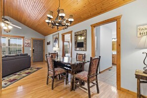 A spacious dining area with a wooden ceiling, a chandelier, and a large table surrounded by chairs. - Blue Sky Lodge  For 4 (Branson West)