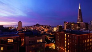 Une vue sur une ville au crépuscule, avec des bâtiments illuminés et un gratte-ciel imposant.